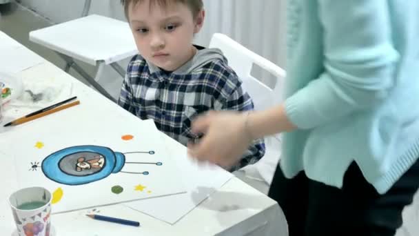 Enfants garçons assis ensemble autour de la table dans la salle de classe et le dessin. Avec eux est leur jeune et beau professeur . — Video