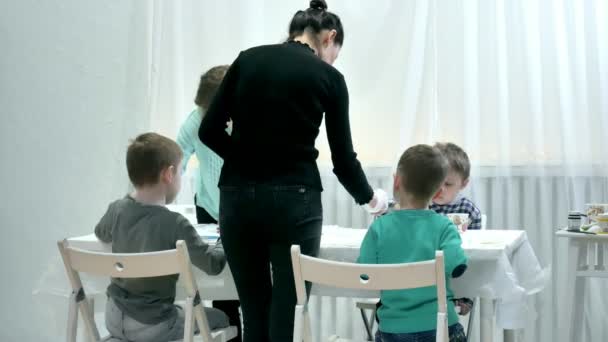 Kinder sitzen zusammen am Tisch im Klassenzimmer und zeichnen. mit ihnen ist ihr junger und schöner Lehrer. — Stockvideo