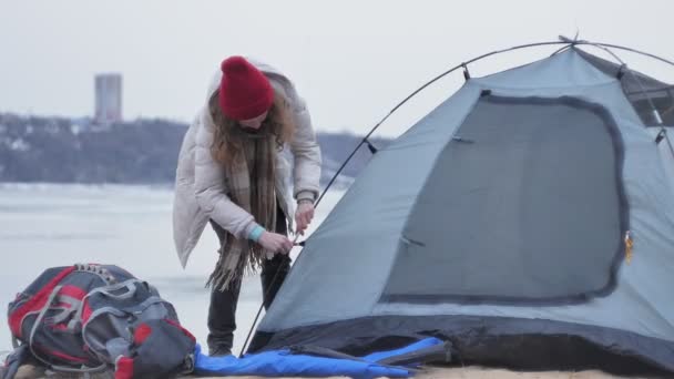 Attraente giovane donna turistica con un cappello rosso raccoglie una tenda turistica vicino alla foresta sulla costa — Video Stock