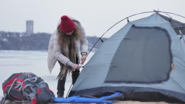 Attraktive junge Touristin mit rotem Hut sammelt ein Touristenzelt am Waldrand an der Küste — Stockvideo