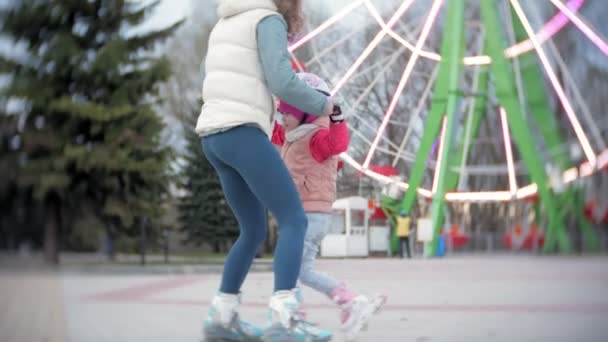 Mom and daughter ride on roller skates. Girl learning to roller skate, and falls. Mom teaches daughter to ride on rollers — Stock Video