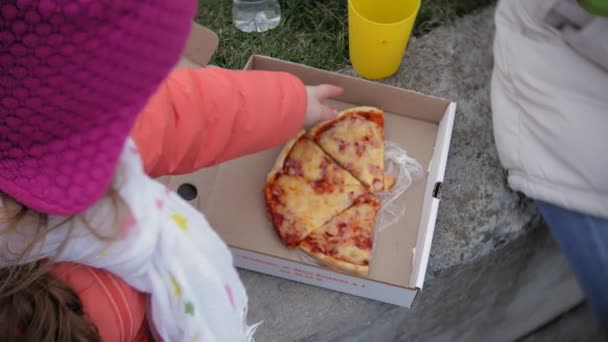 En söt liten tjej och hennes mamma äter pizza utomhus. Näring, mat och livsstil — Stockvideo