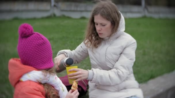 En söt liten tjej och hennes mamma äter pizza utomhus. Näring, mat och livsstil — Stockvideo
