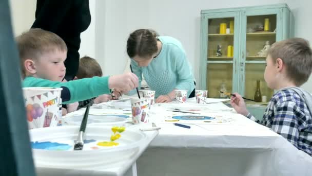 Children boys sitting together around the table in classroom and drawing. With them is their young and beautiful teacher. — Stock Video