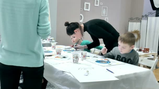 Kinder sitzen zusammen am Tisch im Klassenzimmer und zeichnen. mit ihnen ist ihr junger und schöner Lehrer. — Stockvideo