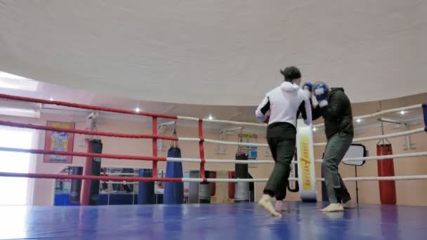 De trainer voert een strijd van de opleiding met een vrouwelijke kickboxer in de ring — Stockvideo