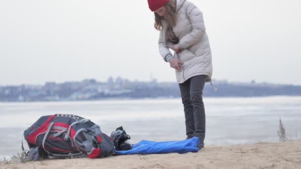 Attraktive junge Touristin mit rotem Hut sammelt ein Touristenzelt am Waldrand an der Küste — Stockvideo
