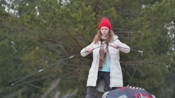 Attraktive junge Touristin mit rotem Hut sammelt ein Touristenzelt am Waldrand an der Küste — Stockvideo