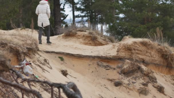 Een aantrekkelijke jonge vrouw in een rode hoed wandelingen door het bos in het vroege voorjaar met een grote toeristische rugzak, dranken thee uit een thermos — Stockvideo