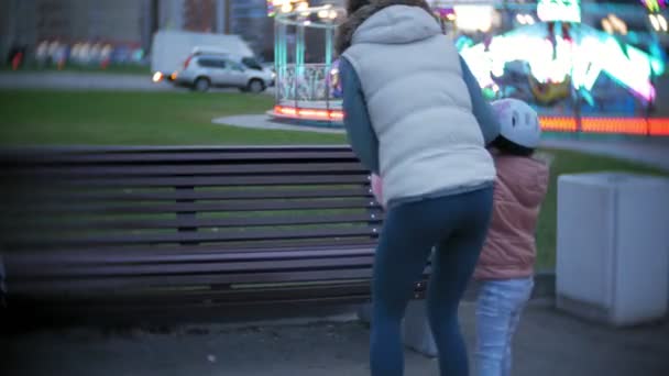 Vacker liten flicka sitter på en bänk i en nöjespark, äta rosa söt sockervadd rullande på rullskridskor — Stockvideo