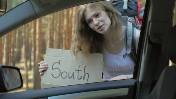 Jeune belle femme auto stop debout sur la route avec un sac à dos sur une table avec une inscription SUD — Video
