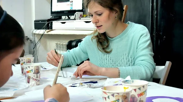 Bambini ragazzi e ragazze seduti insieme intorno al tavolo in classe e disegno. Con loro c'è la loro giovane e bella maestra . — Foto Stock