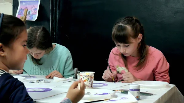 Bambini ragazzi e ragazze seduti insieme intorno al tavolo in classe e disegno. Con loro c'è la loro giovane e bella maestra . — Foto Stock