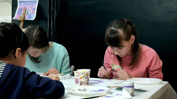 Bambini ragazzi e ragazze seduti insieme intorno al tavolo in classe e disegno. Con loro c'è la loro giovane e bella maestra . — Foto Stock