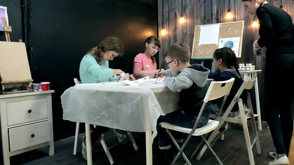 Gyermekek-fiúk és a lányok együtt ül az asztalnál, tantermi és rajz. Velük a fiatal és gyönyörű tanár. — Stock Fotó