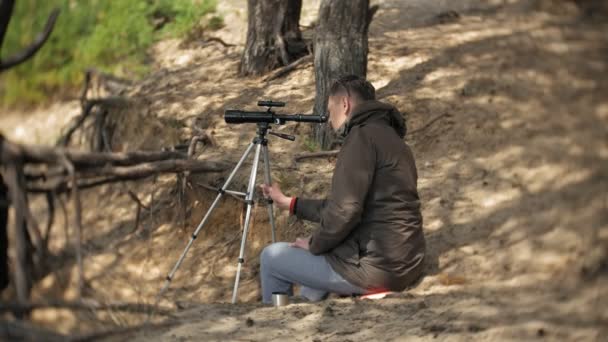 Old man looks through a telescope in a forest on the river bank — Stock Video