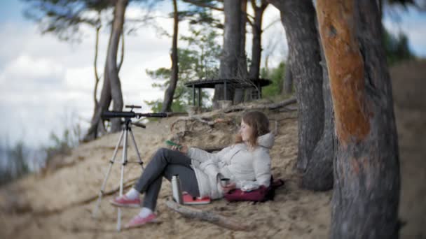 Attractive woman looks through a telescope in a forest on the river bank — Stock Video