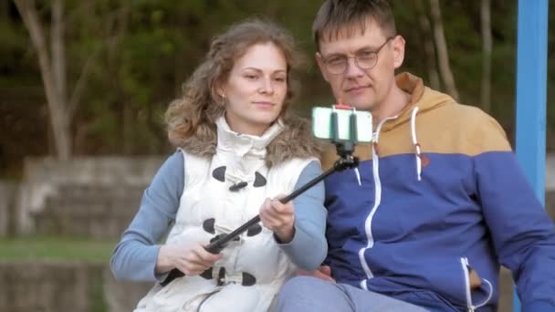 男人发现女人的笑容带着自己的照片自拍手机上的智能手机在公园 — 图库视频影像