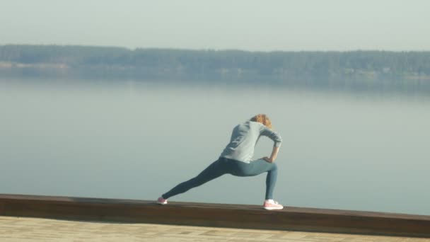 Νέοι γυμναστήριο γυναίκα κάνει ασκήσεις στο γυμναστήριο στην εξωτερική στην όχθη του ποταμού — Αρχείο Βίντεο