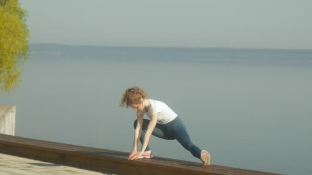 Jovem mulher fitness fazendo exercícios no ginásio em um exterior na margem do rio — Vídeo de Stock