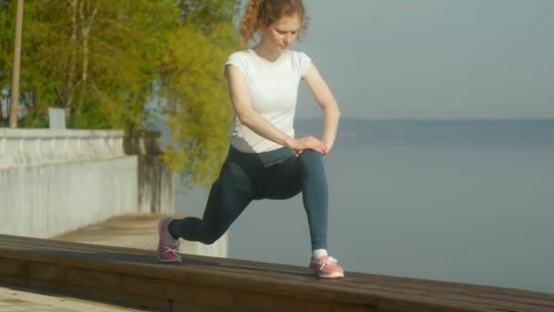 Νέοι γυμναστήριο γυναίκα κάνει ασκήσεις στο γυμναστήριο στην εξωτερική στην όχθη του ποταμού — Αρχείο Βίντεο