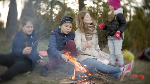 Familia feliz de turistas en un viaje. Mamá y los niños fríen malvaviscos en el fuego cerca de la tienda — Vídeos de Stock