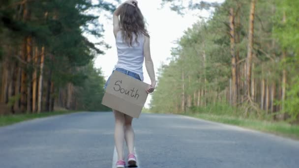 Junge schöne Frau trampt auf der Straße stehend mit einem Rucksack auf einem Tisch mit der Aufschrift Süden — Stockvideo