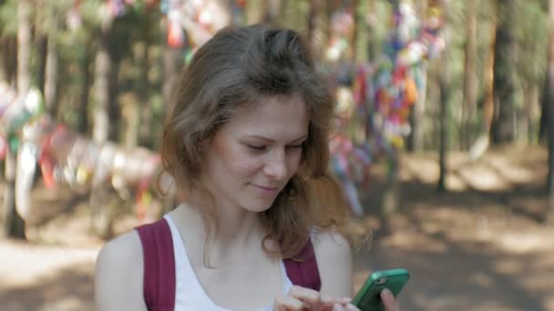 Mujer joven usando un teléfono inteligente en un bosque. Hermosa chica escribiendo en el teléfono en el bosque . — Vídeo de stock