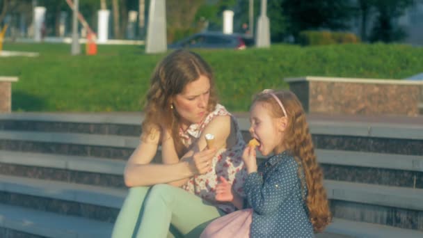 Mom and daughter eating ice cream in a park. mother and child. relaxing happy family — Stock Video