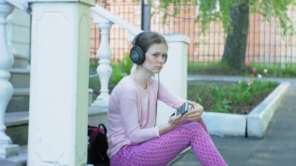 Joven mujer hermosa con estilo, en las calles de la ciudad escuchando música en los auriculares del monitor grande . — Vídeos de Stock