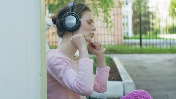 Joven mujer hermosa con estilo, en las calles de la ciudad escuchando música en los auriculares del monitor grande . — Vídeos de Stock