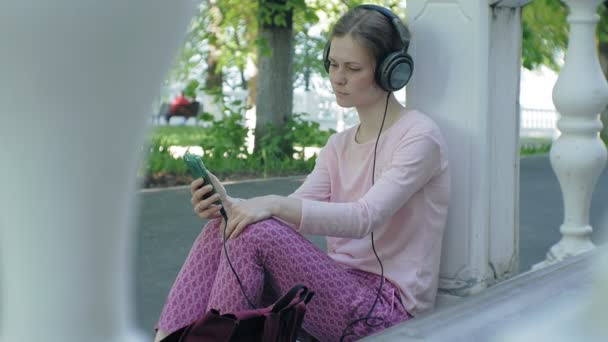 Mladé stylové krásná žena, na ulicích města poslechu hudby ve velkém monitoru sluchátka. — Stock video