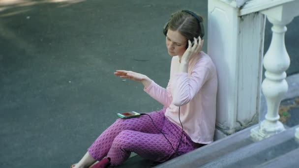 Joven mujer hermosa con estilo, en las calles de la ciudad escuchando música en los auriculares del monitor grande . — Vídeo de stock