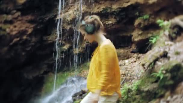 Młoda kobieta piękne stylowe, w pobliżu wodospadu słuchanie muzyki w słuchawkach duży monitor. — Wideo stockowe
