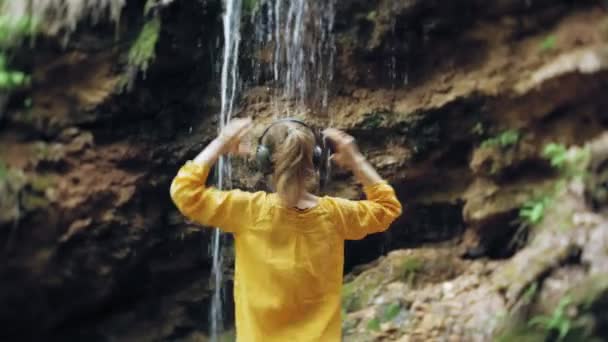 Young stylish beautiful woman, near a waterfall listening to music in large monitor headphones. — Stock Video