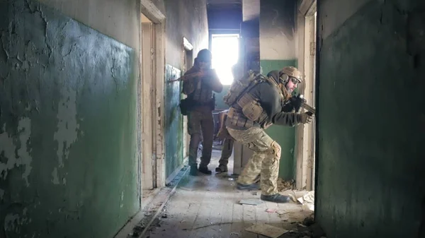 Soldaten in Tarnkleidung mit Kampfwaffen schleichen durch die Gänge des alten Gebäudes, das militärische Konzept — Stockfoto