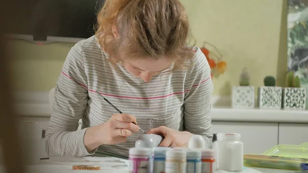 Женщина рисует деревянную куклу цветными красками в своей домашней студии, живопись Матрешки — стоковое фото