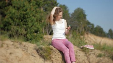 Bir ormanda bir akıllı telefon kullanan genç kadın. Güzel kız ormanda telefonda yazarak.