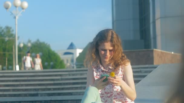 Mujer joven usando un smartphone en un parque. Hermosa chica escribiendo en el teléfono en el bosque . — Vídeos de Stock