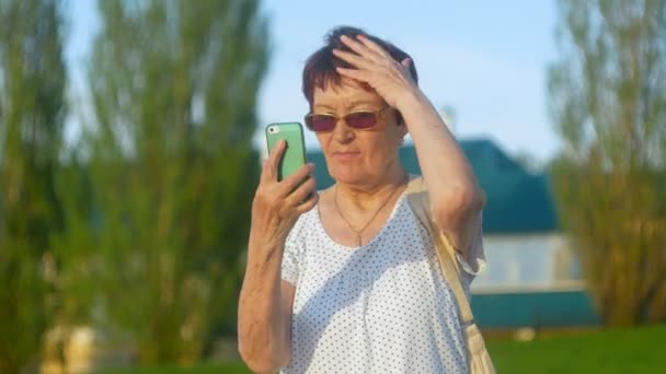 Ler äldre kvinna skriva telefonmeddelande på park. Senior Kvinna med trådlös internetuppkoppling på smart telefon. Glad gammal kvinna tittar på skärmen på smartphone. — Stockvideo