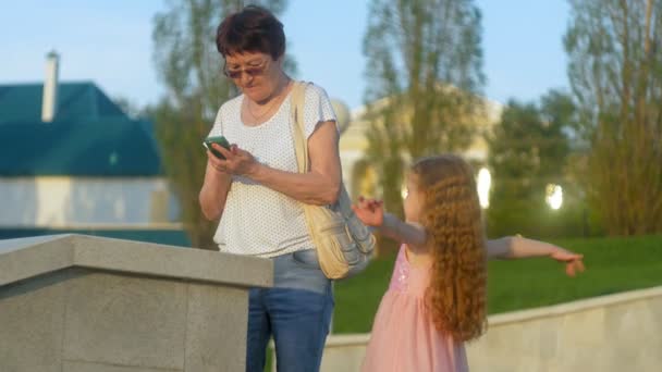微笑的老太太在公园里打手机留言。在智能手机上使用无线互联网连接的高级女士。快乐的老太太看屏幕上的智能手机. — 图库视频影像