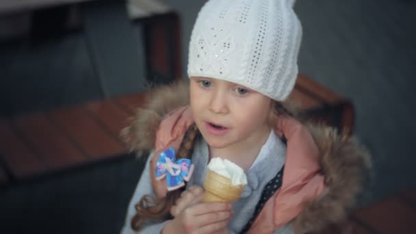 Roztomilé batole dívka v bílé pletené čepice jíst zmrzlinu — Stock video