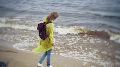 Sahil boyunca seyahat yaşam tarzı macera tatil açık havada yürüyen mutlu kadın. Bir moda sarı yağmurluk giymiş bir kız