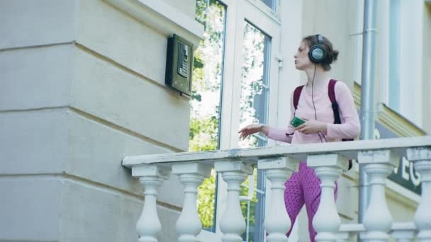 Stijlvolle mooie jongedame, op de straten van de stad luisteren naar muziek in de grote monitor hoofdtelefoon. — Stockvideo