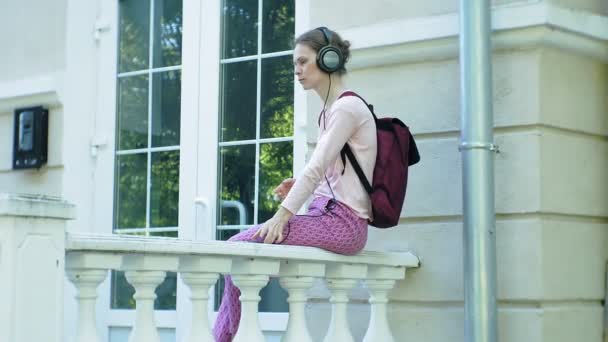 Joven mujer hermosa con estilo, en las calles de la ciudad escuchando música en los auriculares del monitor grande . — Vídeo de stock