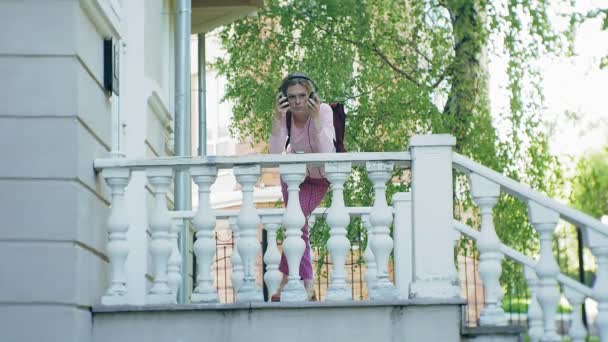 Joven mujer hermosa con estilo, en las calles de la ciudad escuchando música en los auriculares del monitor grande . — Vídeos de Stock