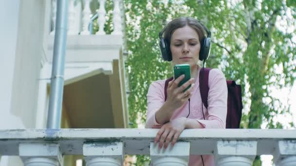 Jeune belle femme élégante, dans les rues de la ville à l'écoute de la musique dans les écouteurs grand moniteur . — Video