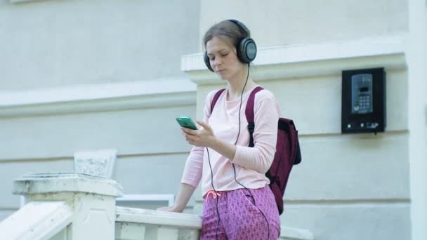 Joven mujer hermosa con estilo, en las calles de la ciudad escuchando música en los auriculares del monitor grande . — Vídeos de Stock