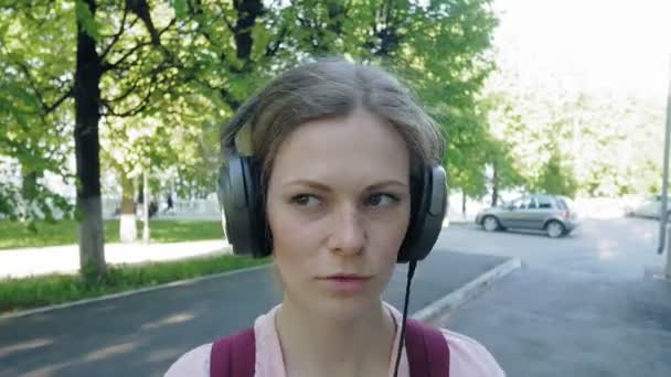 Giovane bella donna alla moda, per le strade della città ad ascoltare musica in cuffie monitor di grandi dimensioni . — Video Stock