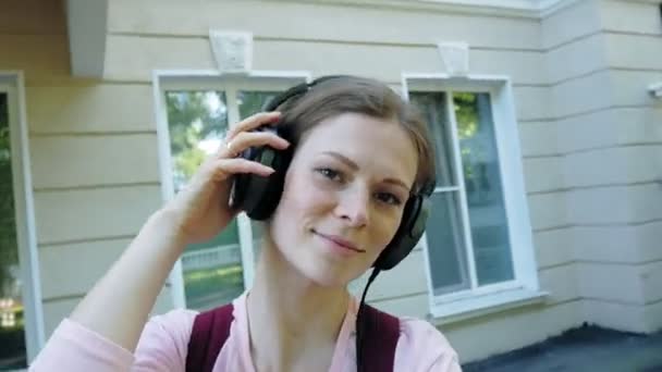 Κομψό όμορφη γυναίκα, στους δρόμους της πόλης να ακούτε μουσική στα ακουστικά μεγάλη οθόνη. — Αρχείο Βίντεο
